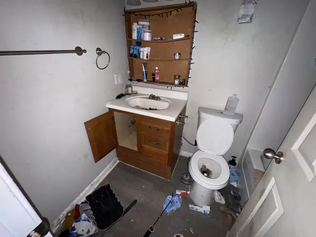 Bathroom with an open vanity and trash on the floor