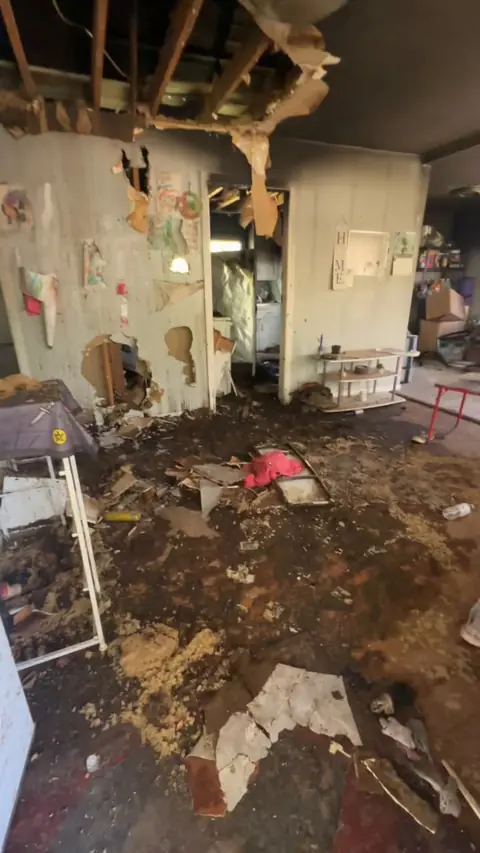 Living room with the ceiling burned open to the rafters and debris on the floor