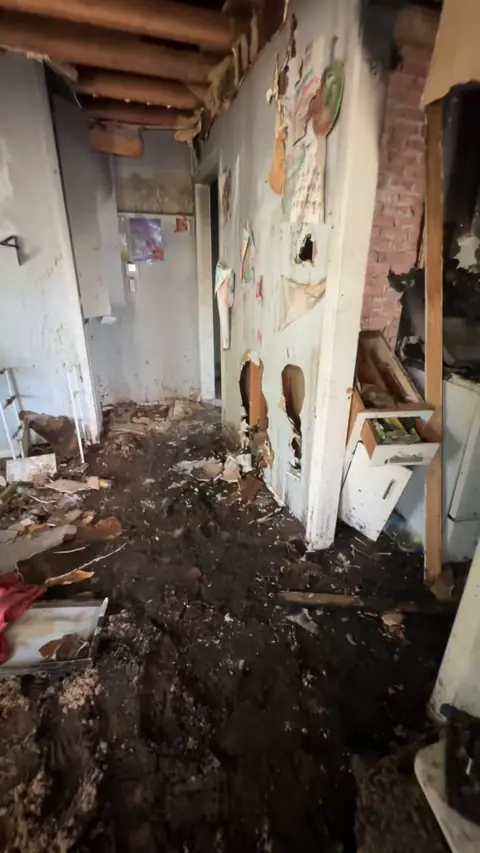 Hallway with burned walls, an open ceiling, and debris on the floor